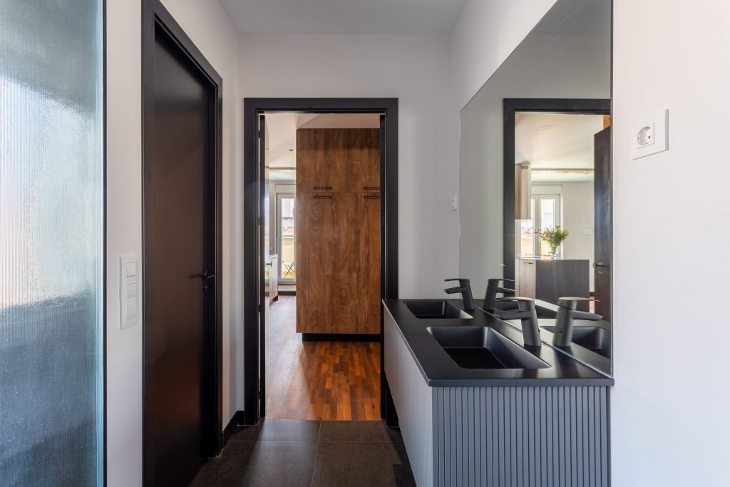 Vista de baño abierto a la habitación. Con mueble lavabo de doble seno con espejo y mampara de ducha.