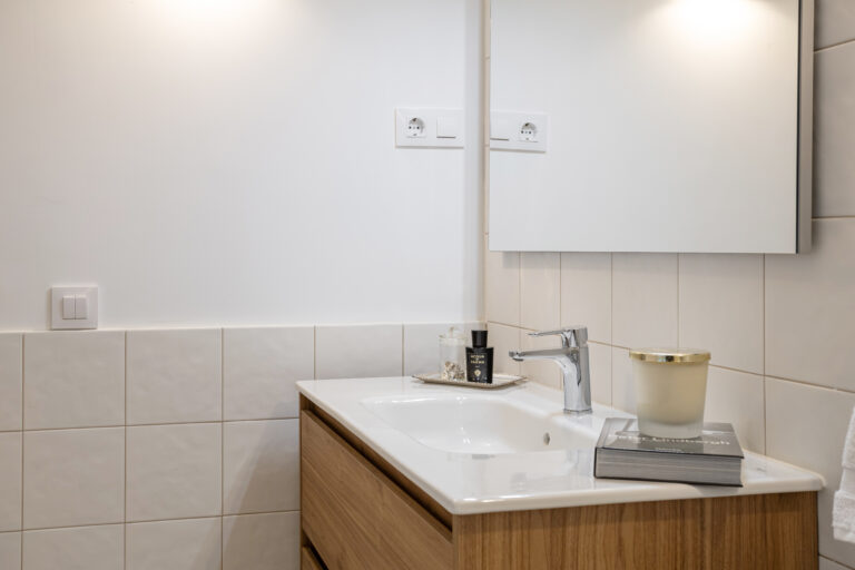 Vista de mueble lavabo con velas y perfume sobre encimera.