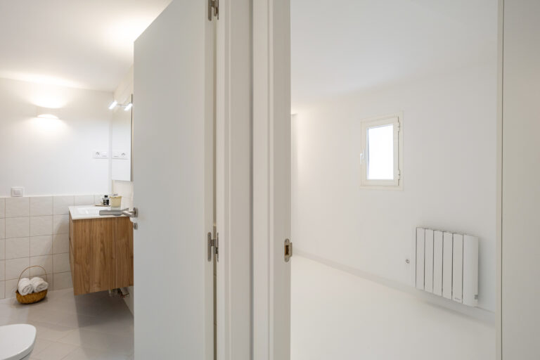 Paso a baño y dormitorio, con mueble lavabo suspendido y cesta con toallas en el suelo.