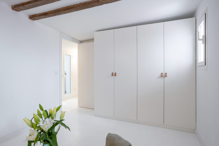 Armario blanco de Ikea en habitación blanca con vigas de madera y flores blancas